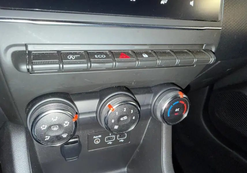 Gros plan sur la console centrale noire de la Renault Clio 2023 avec commandes climatisation et prises audio USB.