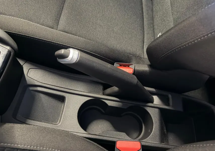 Vue en plongée sur le frein à main et porte-gobelets noirs entre les sièges avant d'une Renault Clio gris platine.