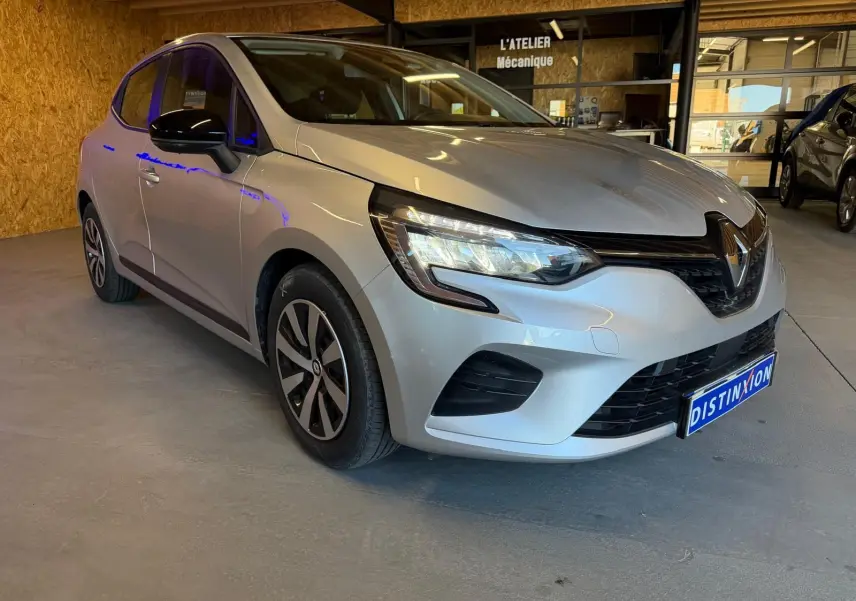 Renault Clio gris platine vue 3/4 avant droit en intérieur avec phares LED et jantes stylisées.