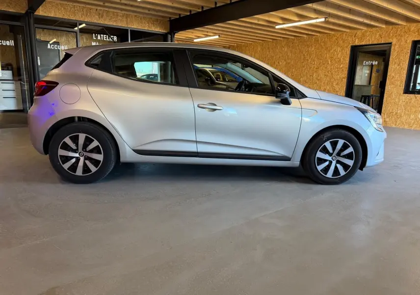 Profil droit d'une Renault Clio gris platine 2023, avec enjoliveurs noirs et poignées ton carrosserie visibles.