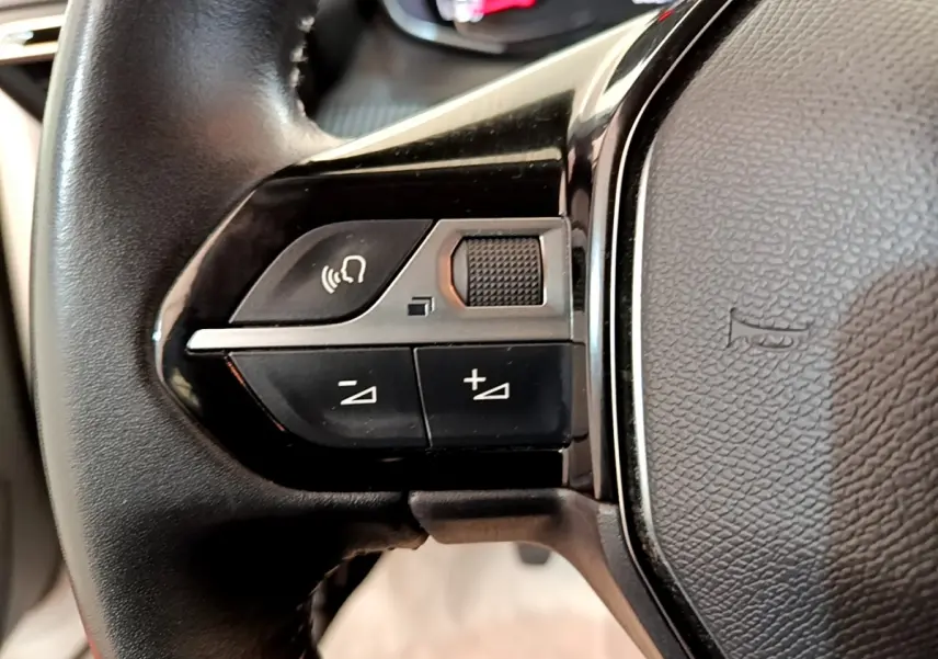 Gros plan sur les commandes gauche du volant cuir multifonctions du Peugeot 2008 blanc, version BlueHDi 110 S&S Active Business.