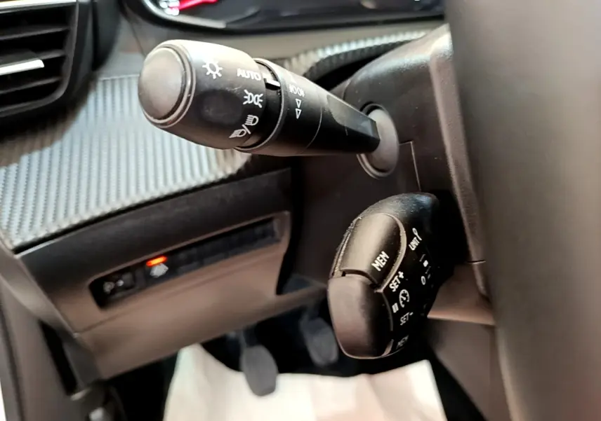 Gros plan sur les commandes de phares et régulateur de vitesse à gauche du volant dans l’habitacle d’un Peugeot 2008 blanc.