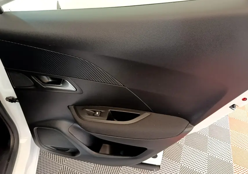 Vue intérieure du panneau de porte avant gauche de la Peugeot 2008 blanc, avec commande de vitre et poignée argentée.