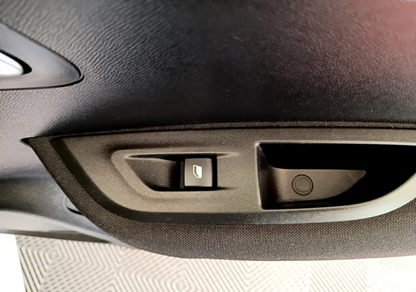 Gros plan sur le bouton d'ouverture de coffre intégré dans le panneau intérieur noir d'une Peugeot 2008 blanche.