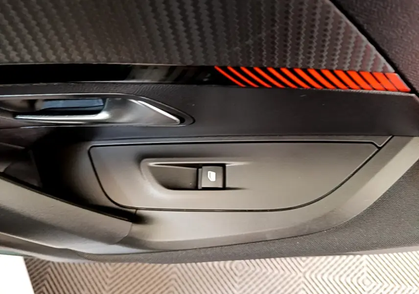 Détail de la porte intérieure côté conducteur du Peugeot 2008 blanc, avec bouton de commande de vitre et insert décoratif rouge.