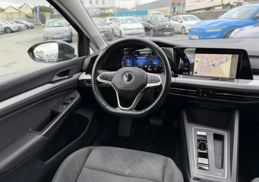 Vue intérieure avant gauche de la Volkswagen Golf SW 2.0 TDI gris, avec tableau de bord digital et écran tactile navigation.