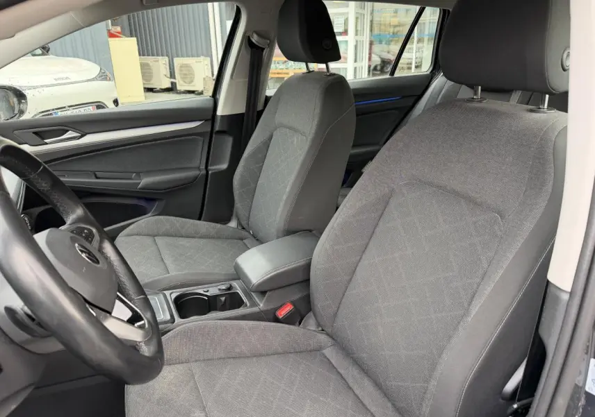 Vue intérieure côté avant gauche de la Volkswagen Golf SW 2.0 TDI gris avec sièges tissu Maze et accoudoir central.