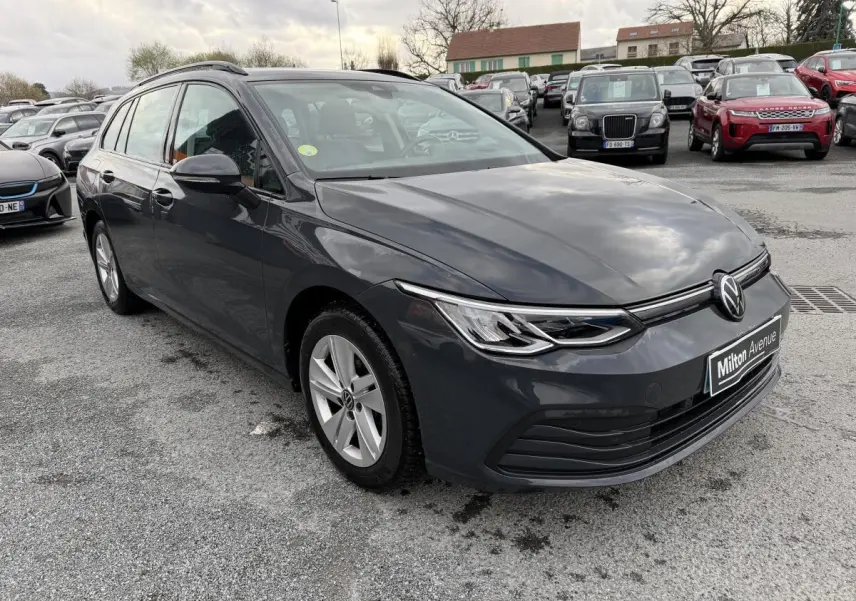 Volkswagen Golf SW gris vue 3/4 avant droit, jantes alliage et calandre épurée sous ciel nuageux.