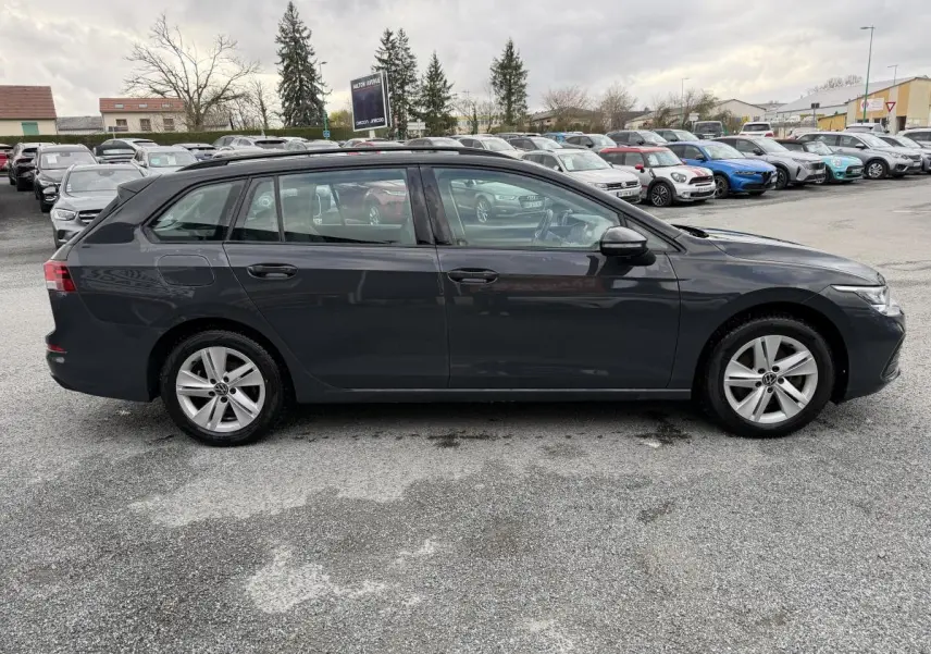 Vue latérale droite d'une Volkswagen Golf SW gris foncé stationnée sur un parking avec plusieurs autres véhicules en arrière-plan.