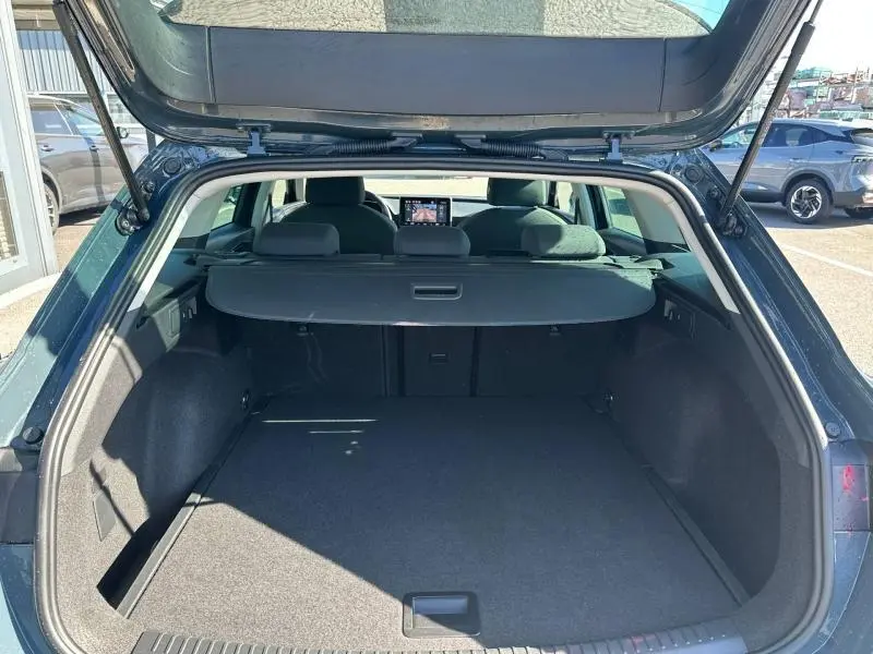 Vue arrière du coffre ouvert d'une SEAT LEON ST 2.0 TDI 115ch STYLE XL bleu saphir métallisé, montrant l'espace de chargement et l'intérieur.