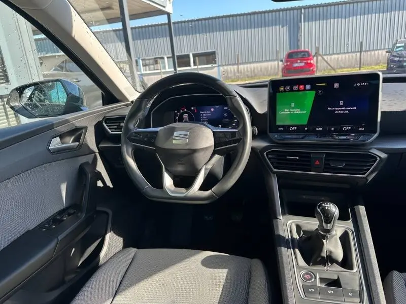 Vue intérieure frontale du poste de conduite d'une SEAT LEON ST 2025 avec volant multifonction, écran tactile et levier de vitesses manuel.