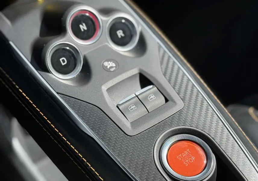 Gros plan sur la console centrale en carbone de l'Alpine A110 1.8T 292 S avec bouton start/stop rouge et surpiqûres orange.