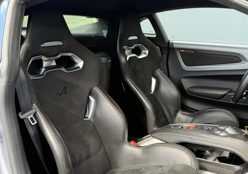 Vue intérieure côté gauche des sièges baquets noirs en cuir et Dinamica avec surpiqûres orange de l'Alpine A110 Gris Tonnerre Mat.