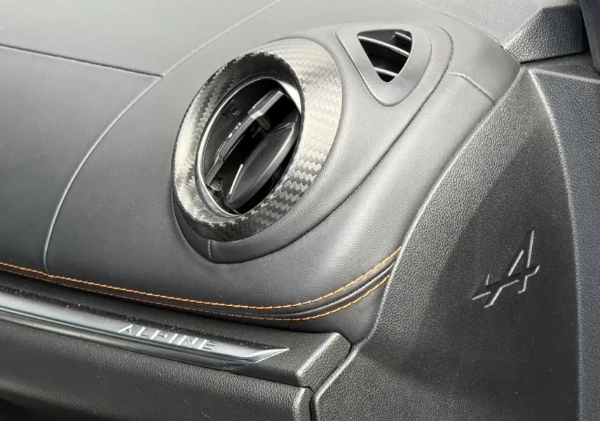 Détail intérieur côté passager de l'Alpine A110 gris mat, avec sortie d'air carbone et surpiqûres orange.