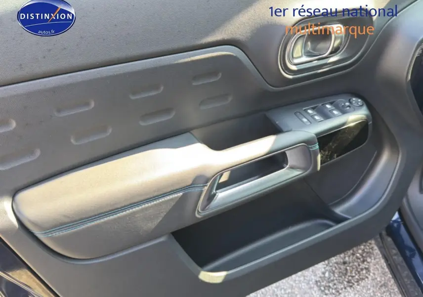 Vue intérieure côté gauche de la porte avant d’un Citroën C5 Aircross bleu eclipse avec commandes de vitres et poignée intégrée.