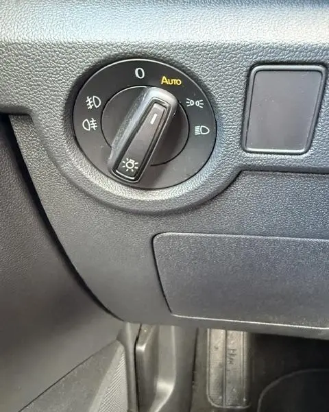 Gros plan sur le bouton de commande des feux avec mode automatique dans l’habitacle gris foncé du Volkswagen T-Cross 2023.