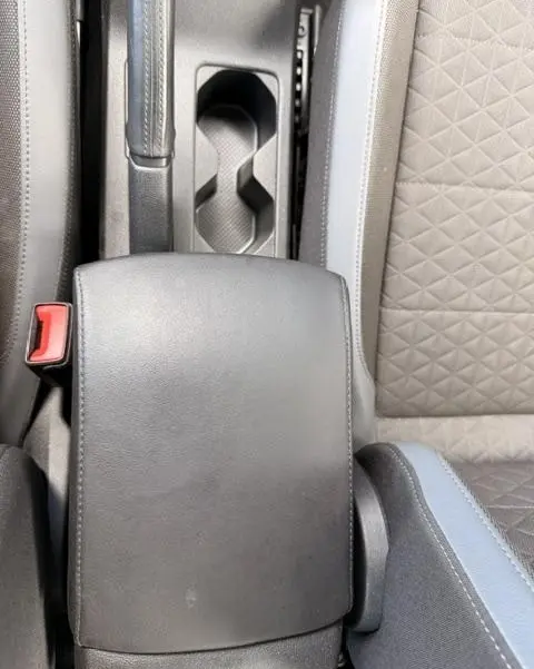 Vue plongeante sur l'accoudoir central en cuir noir et les sièges tissu gris du Volkswagen T-Cross 2023.