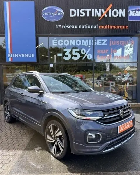 Vue 3/4 avant d'un Volkswagen T-Cross gris foncé R-Line Tech 2023 avec jantes alliage et badge R-Line visible.