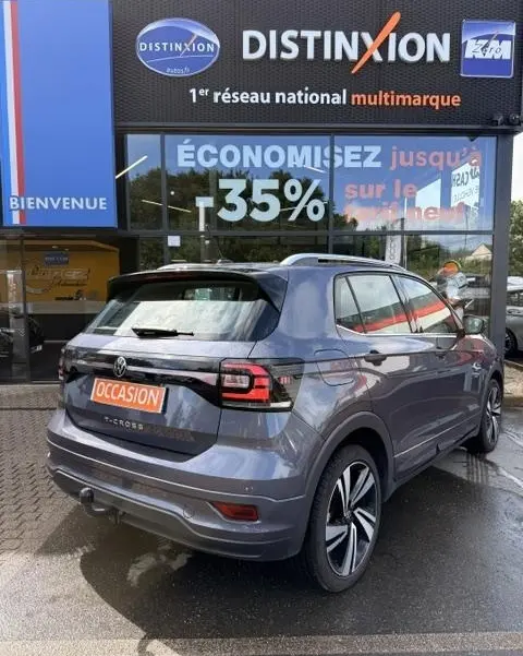 Vue 3/4 arrière droite d'un Volkswagen T-Cross gris foncé 2023 avec finition R-Line devant un concessionnaire multimarque.