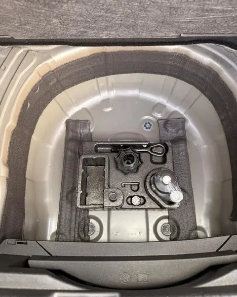 Vue en plongée sur le coffre gris foncé du Volkswagen T-Cross 2023, montrant le rangement d’outils et l’emplacement de la roue de secours.