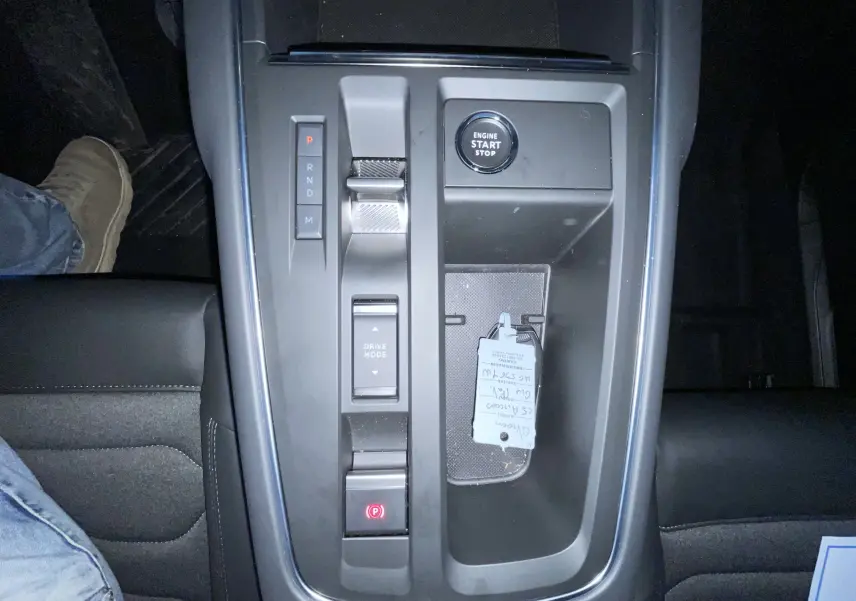 Gros plan sur les commandes noires du tableau de bord du Citroën C5 Aircross hybride 2025, réglage des phares et aides à la conduite.