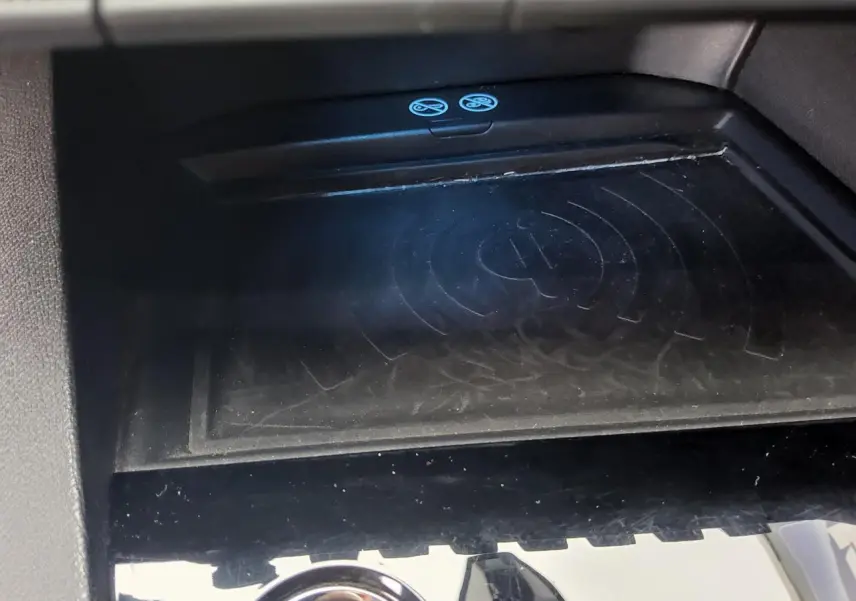 Surface de recharge sans fil noire dans l'habitacle du Peugeot 3008 rouge foncé, vue rapprochée du compartiment central.