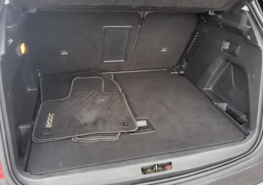 Coffre ouvert d’un Peugeot 3008 rouge foncé, vue intérieure montrant tapis de sol et espace de rangement.