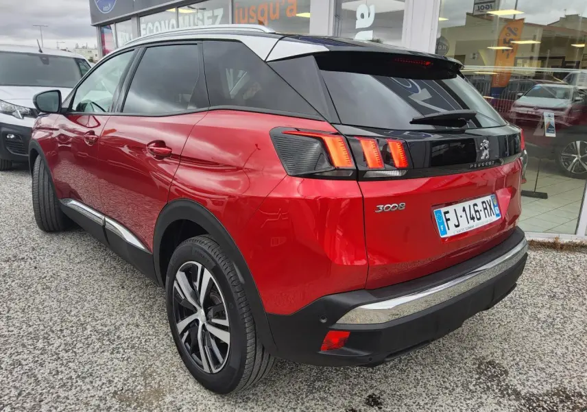 Vue 3/4 arrière droite d’un Peugeot 3008 rouge foncé avec toit noir et jantes alliage bi-ton, garé devant un showroom.