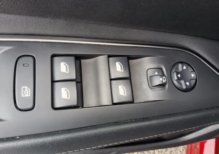 Gros plan sur les commandes des vitres et rétroviseurs côté conducteur du Peugeot 3008 rouge foncé, intérieur noir.
