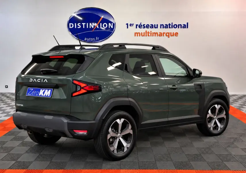 Vue 3/4 arrière droite du Dacia Duster 2026 vert cèdre avec jantes alliage et barres de toit noires.