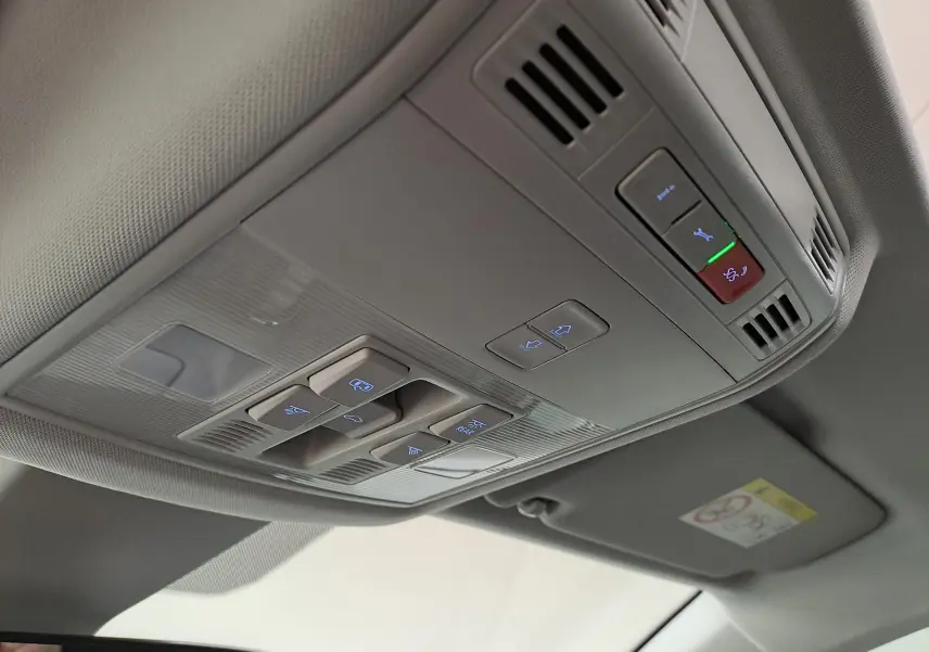 Vue intérieure en plongée sur la console de toit gris clair du Skoda Karoq 2023 avec commandes éclairées du toit ouvrant panoramique.