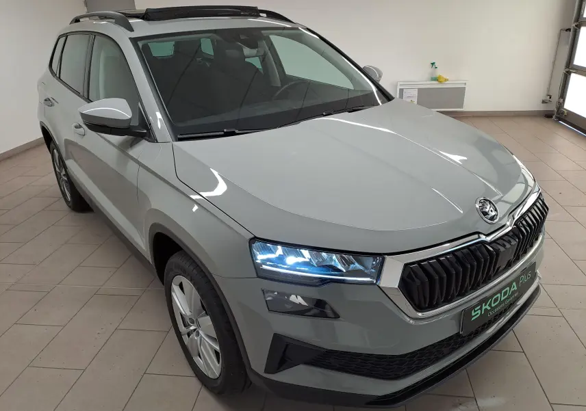 Vue 3/4 avant gauche d'un Skoda Karoq gris perle avec toit ouvrant panoramique et phares allumés en intérieur.