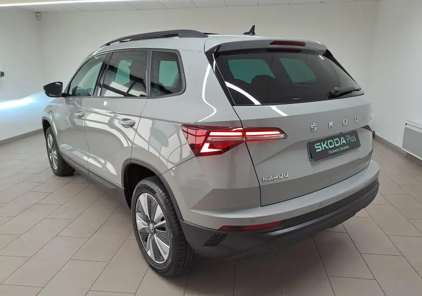 Vue 3/4 arrière droite d’un Skoda Karoq gris perle avec toit ouvrant panoramique dans un showroom.