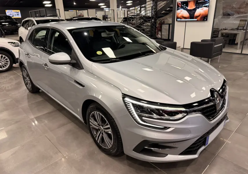 Renault Mégane IV gris Highland vue 3/4 avant droit en showroom, avec phares LED et jantes alliage.