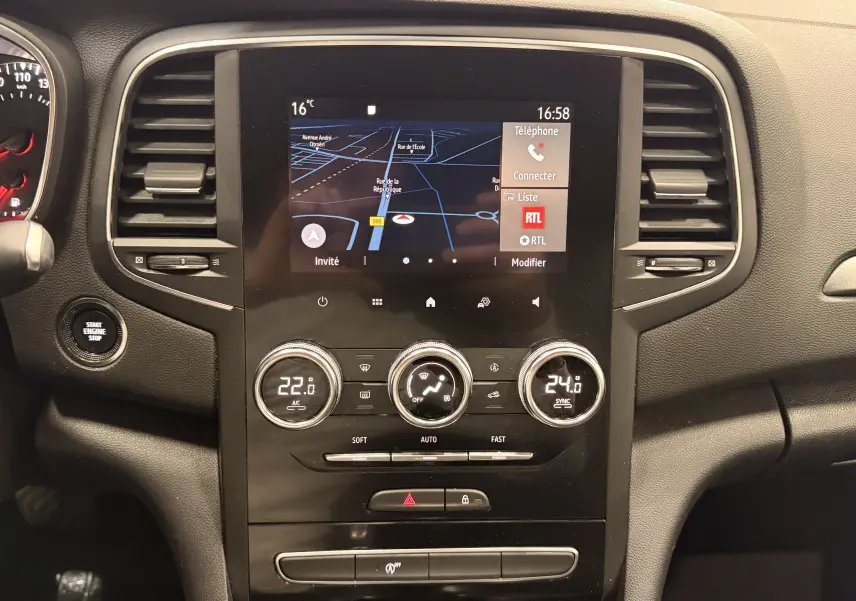 Vue rapprochée du tableau de bord noir de la Renault Mégane IV avec écran tactile et commandes de climatisation digitales.