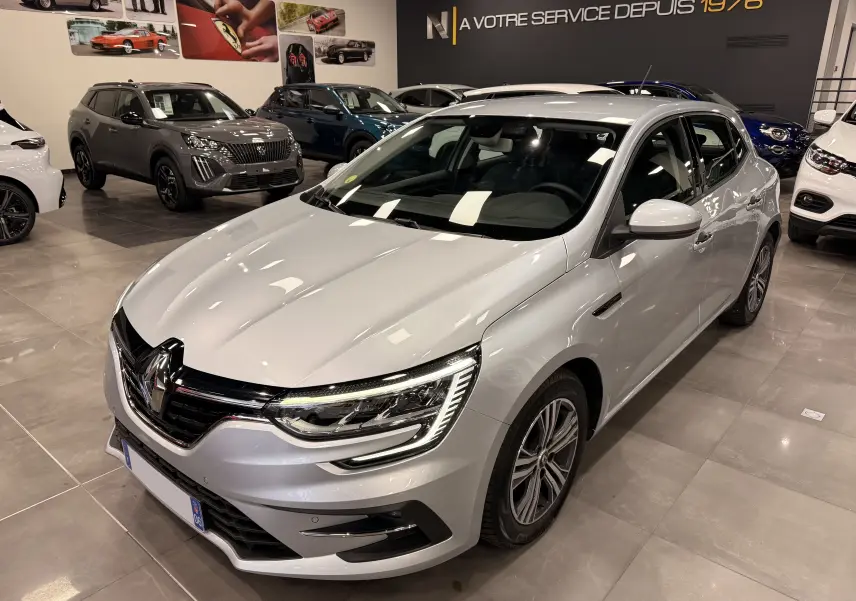 Renault Mégane IV gris Highland vue 3/4 avant droit, avec feux LED et calandre noire brillante en showroom.