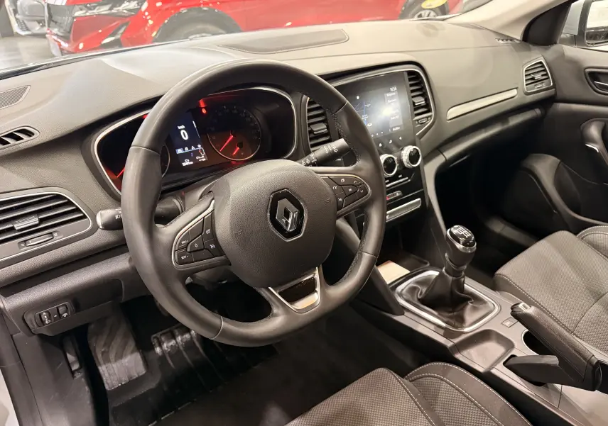 Vue intérieure côté conducteur de la Renault Mégane IV gris Highland, volant multifonction et levier de vitesse manuel visibles.