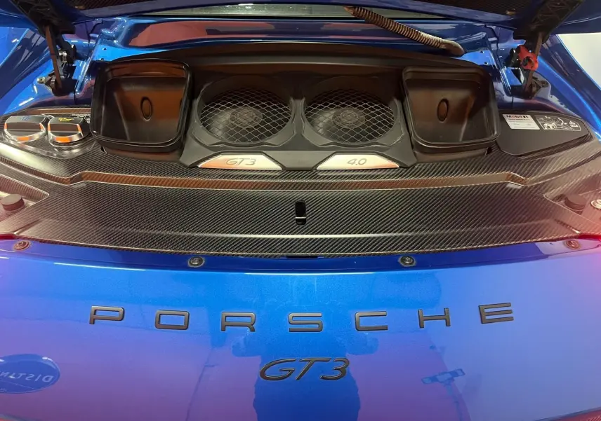 Vue rapprochée du compartiment moteur arrière d’une Porsche 911 GT3 bleu saphir avec détails en carbone et logos GT3 4.0 visibles.