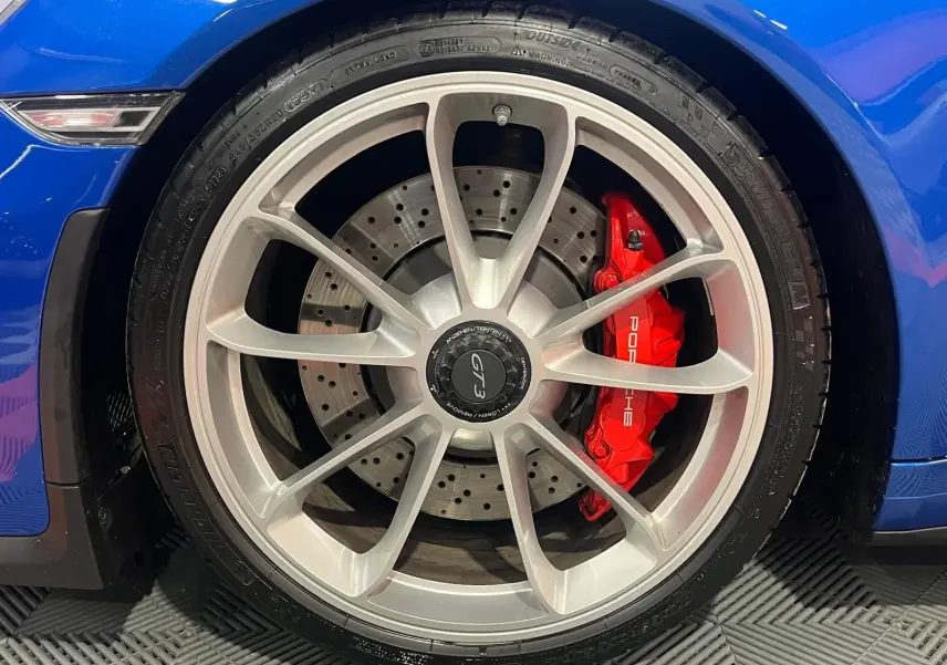 Gros plan sur la roue avant gauche d'une Porsche 911 GT3 bleu saphir avec étrier de frein rouge et jante argentée.