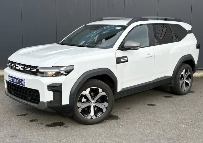 Dacia Bigster blanc Banquise en 3/4 avant droit, avec barres de toit gris et jantes alliage 18 pouces diamantées.