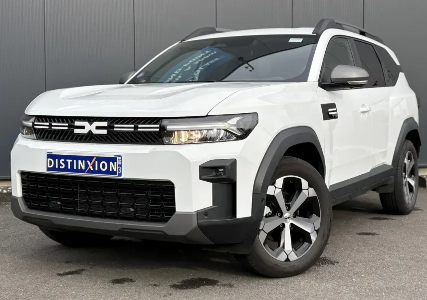 Vue 3/4 avant droit du Dacia Bigster blanc Banquise avec jantes alliage et barres de toit gris mégalithe.