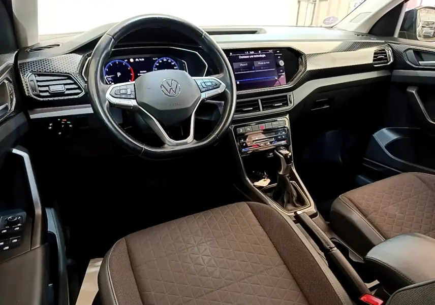 Vue intérieure avant du Volkswagen T-Cross 2022, montrant le volant multifonctions, tableau de bord digital et sièges tissu marron.