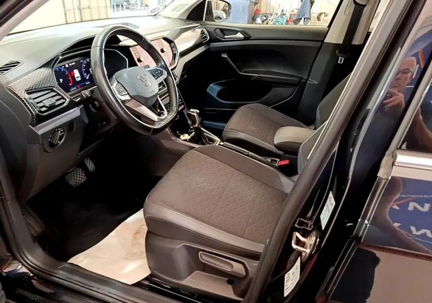 Intérieur avant côté conducteur du Volkswagen T-Cross noir, avec tableau de bord digital et sièges tissu gris.