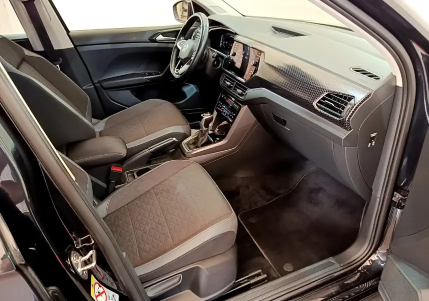 Vue intérieure côté conducteur du Volkswagen T-Cross noir, mettant en valeur le tableau de bord moderne et les sièges tissu gris.