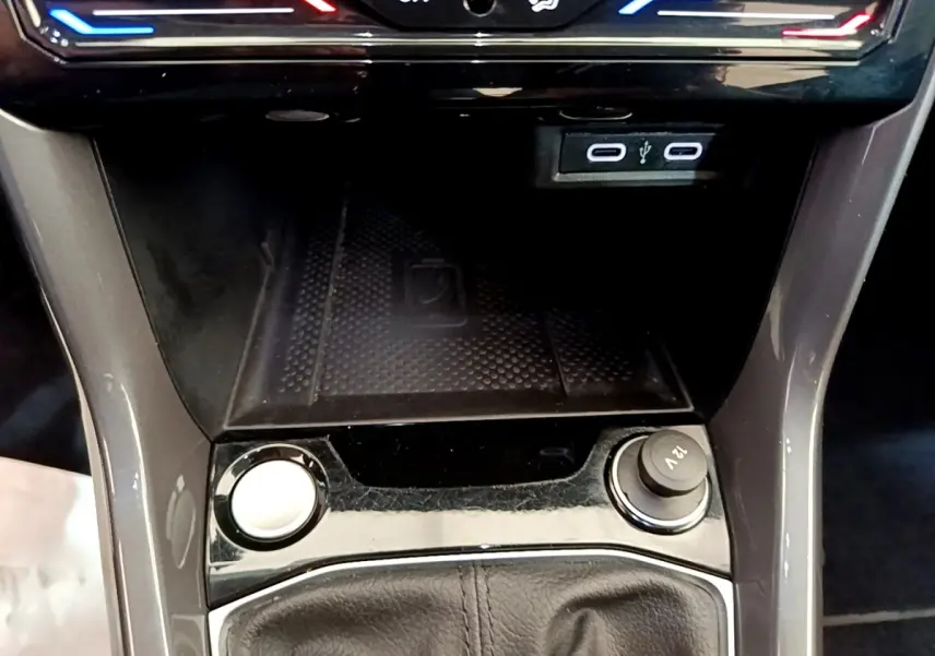 Vue rapprochée de la console centrale du Volkswagen T-Cross noir, avec zone de recharge sans fil et prises USB visibles.