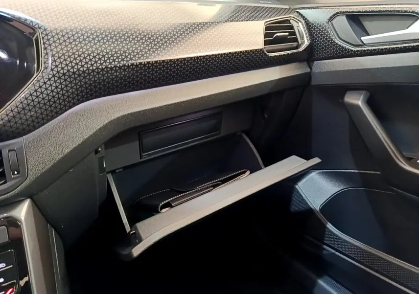 Intérieur noir du Volkswagen T-Cross 2022, vue sur la boîte à gants ouverte côté passager avec tableau de bord texturé.