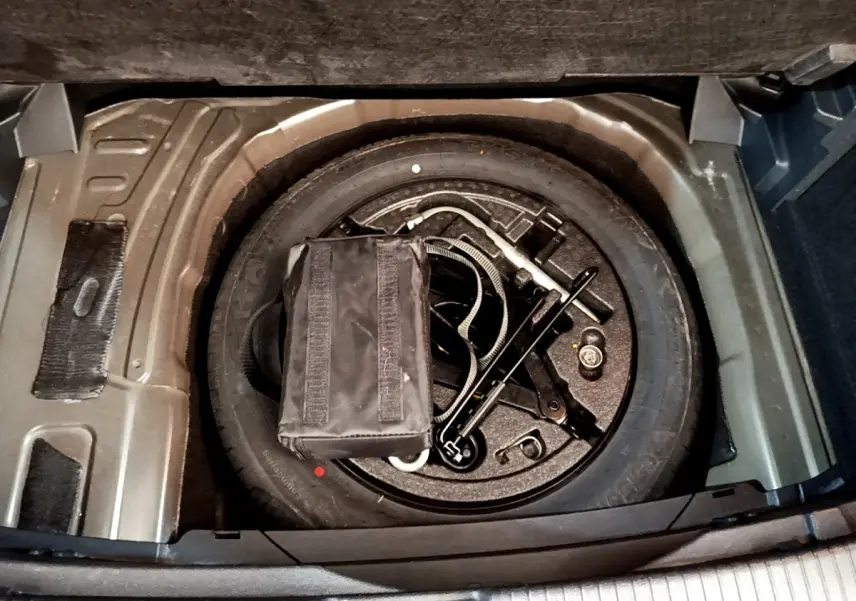 Vue plongeante sur la roue de secours et outils dans le coffre du Volkswagen T-Cross noir, version 2022.