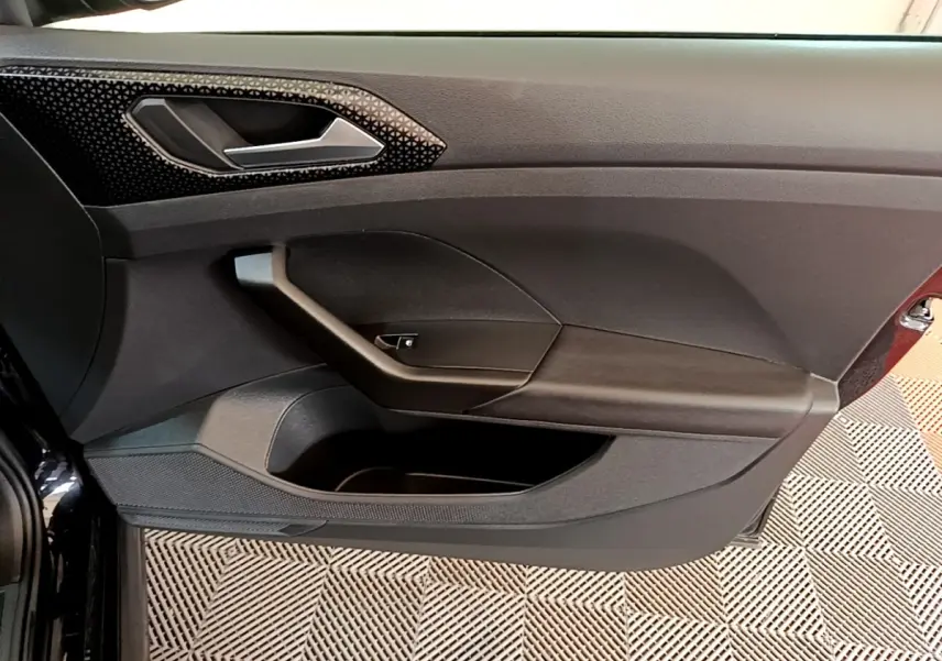 Vue rapprochée de la porte intérieure côté conducteur du Volkswagen T-Cross noir, avec poignée et rangement intégré.