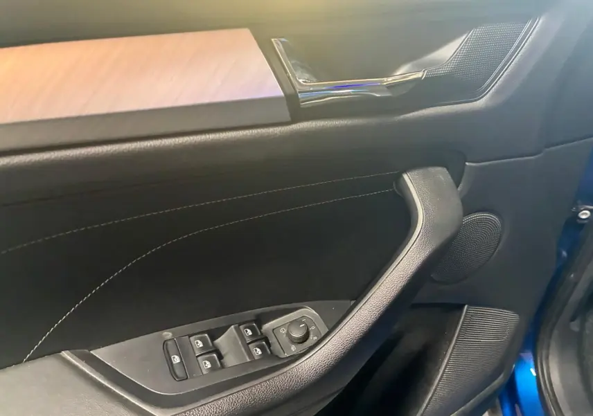 Détail de la porte avant gauche du Skoda Kodiaq bleu 2023, montrant les commandes des vitres et le revêtement noir avec surpiqûres.