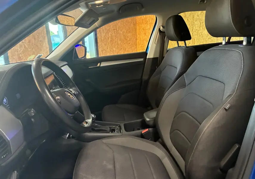 Vue intérieure côté conducteur du Skoda Kodiaq bleu 2023, mettant en valeur les sièges noirs en tissu et le volant multifonction.